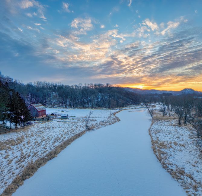 A peaceful winter sunset over a snow-covered landscape with a barn and river in Tell, Wisconsin.