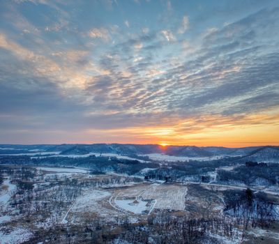 Breathtaking winter sunset over a snow-covered rural landscape in Tell, Wisconsin, revealing a serene and vivid horizon.