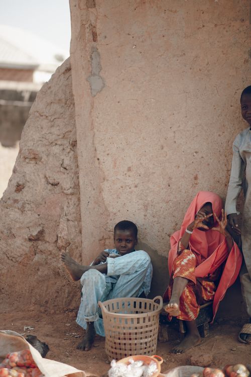 Free Children sit by a wall at a sunlit market, conveying a serene and vibrant atmosphere. Stock Photo