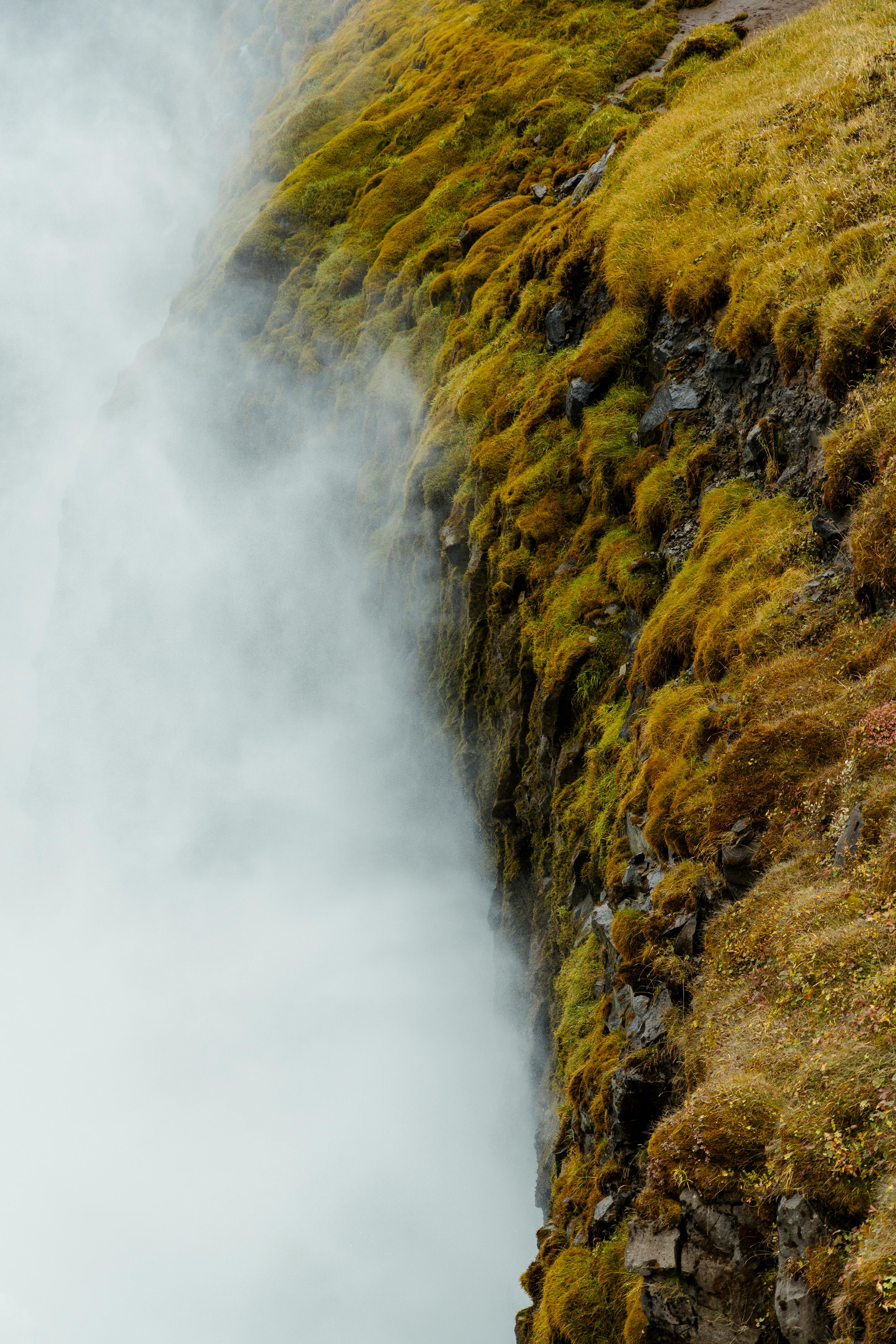 Captured in Iceland, this misty waterfall cascades over vibrant moss-covered cliffs, showcasing nature's raw beauty.