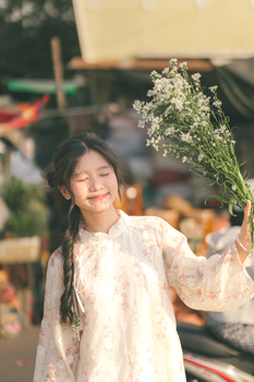 Smiling woman in Asian attire holding flowers, enjoying sunny day outdoors.