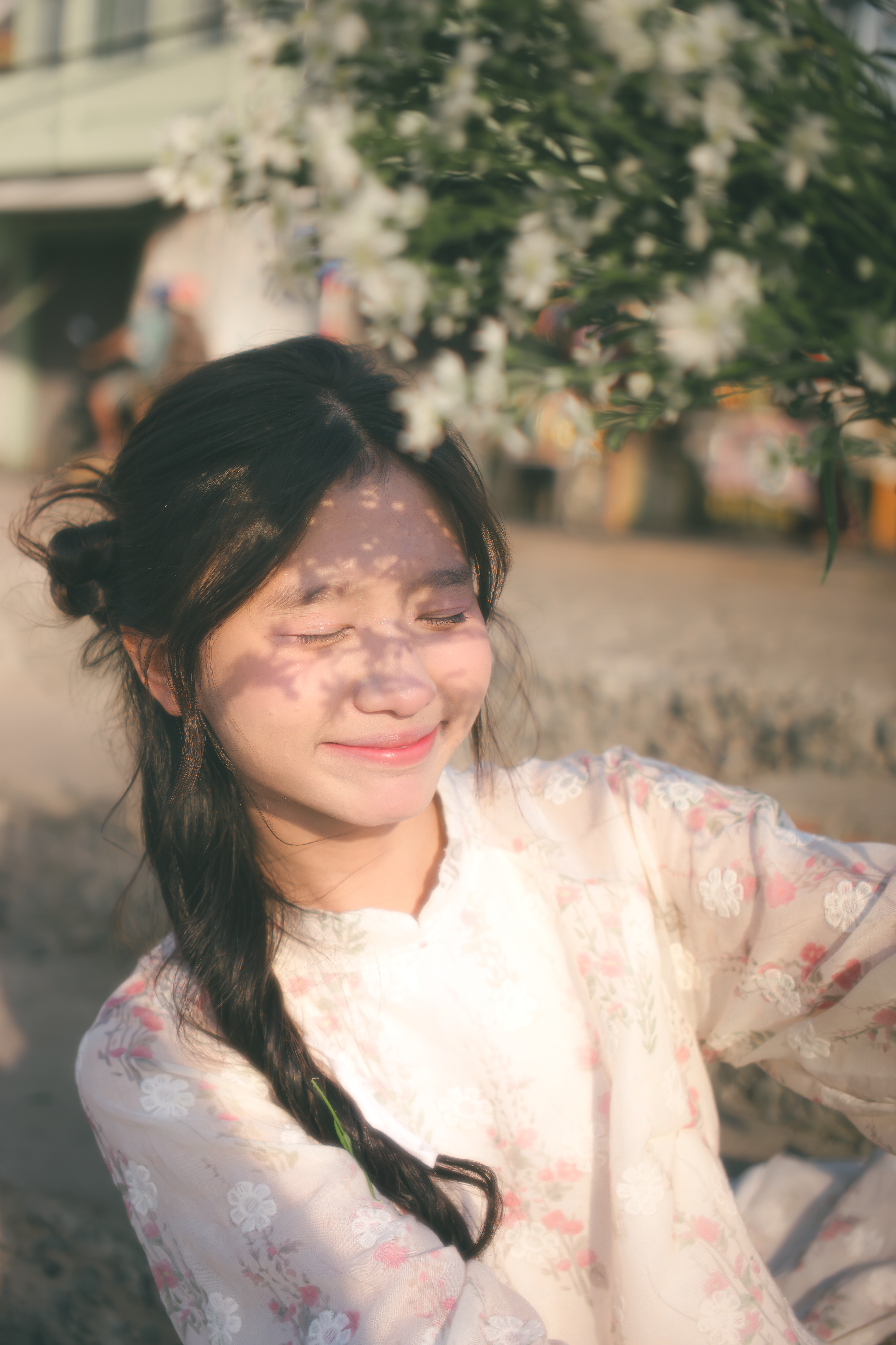 Young woman smiling outdoors in sunlight with floral shadows on face.