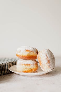 A delicious stack of fluffy powdered sugar donuts on a plate, perfect for dessert enthusiasts.