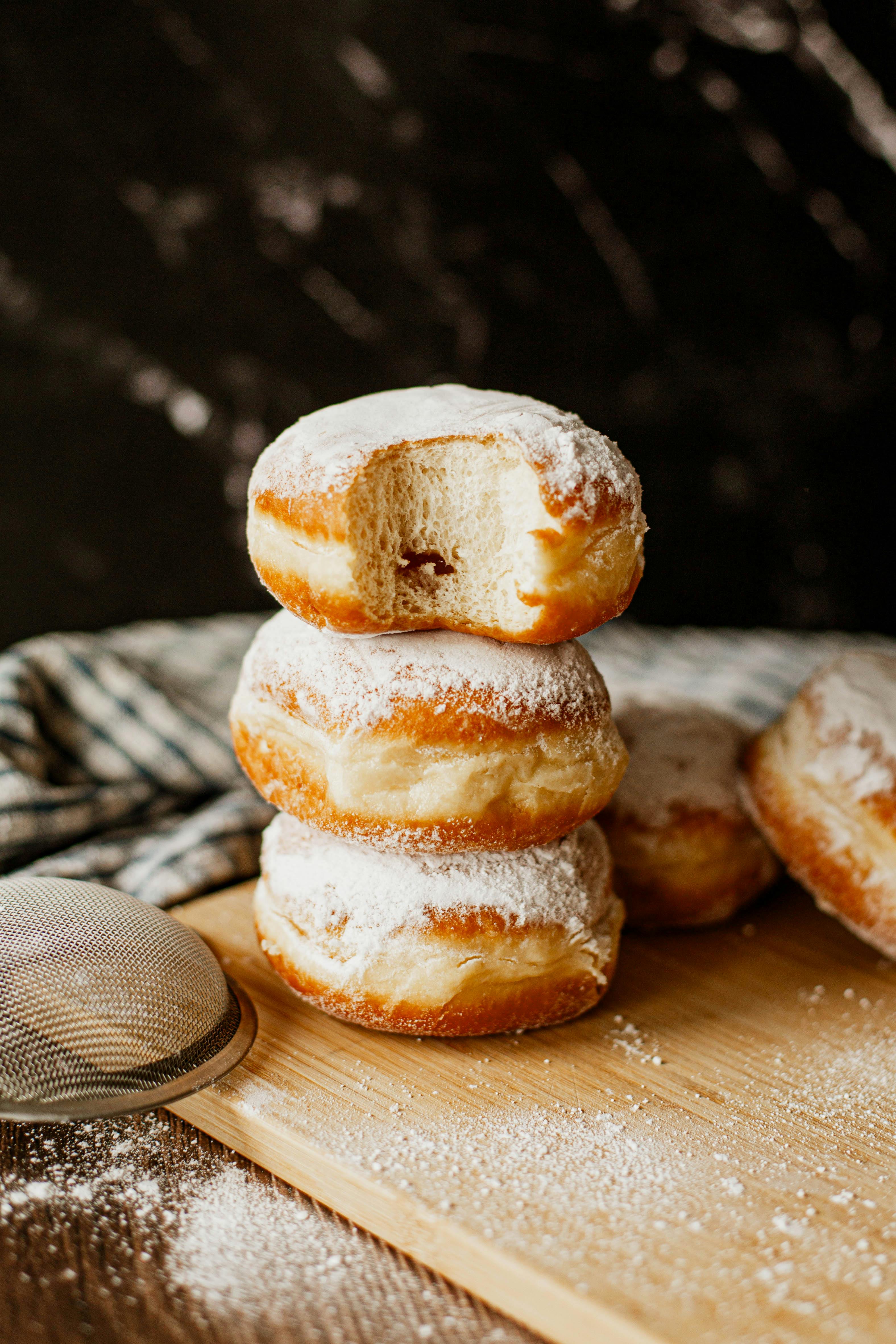 Stack of delicious powdered sugar donuts on a wooden board with cozy kitchen ambiance.