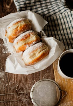 Three donuts with powdered sugar paired with a cup of black coffee, captured in warm natural light.