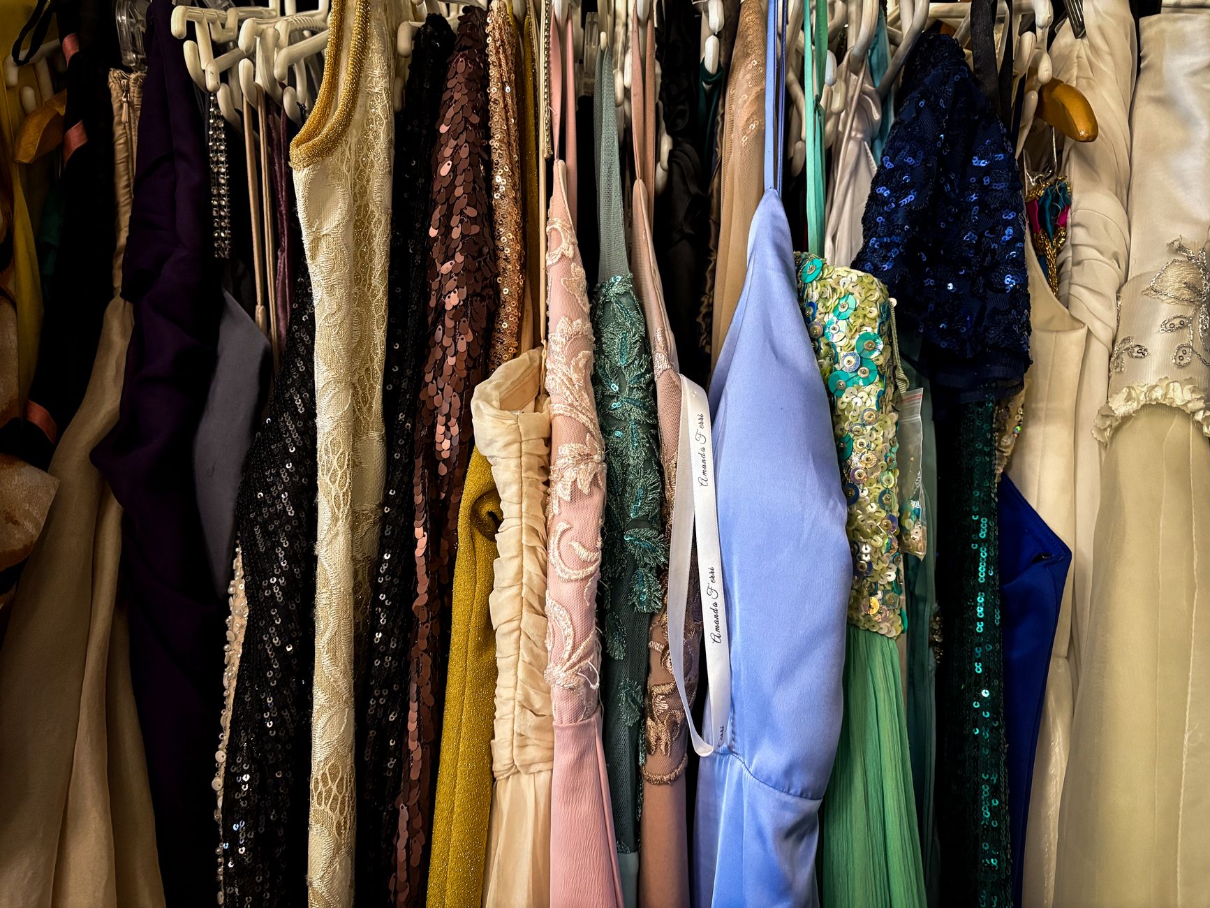 Rows of vintage dresses hanging tightly together on a rack, suggesting the archive behind a rental wardrobe