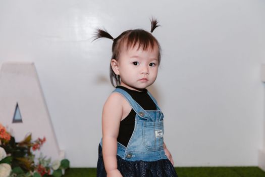 Adorable toddler with pigtails wearing a denim dress indoors.