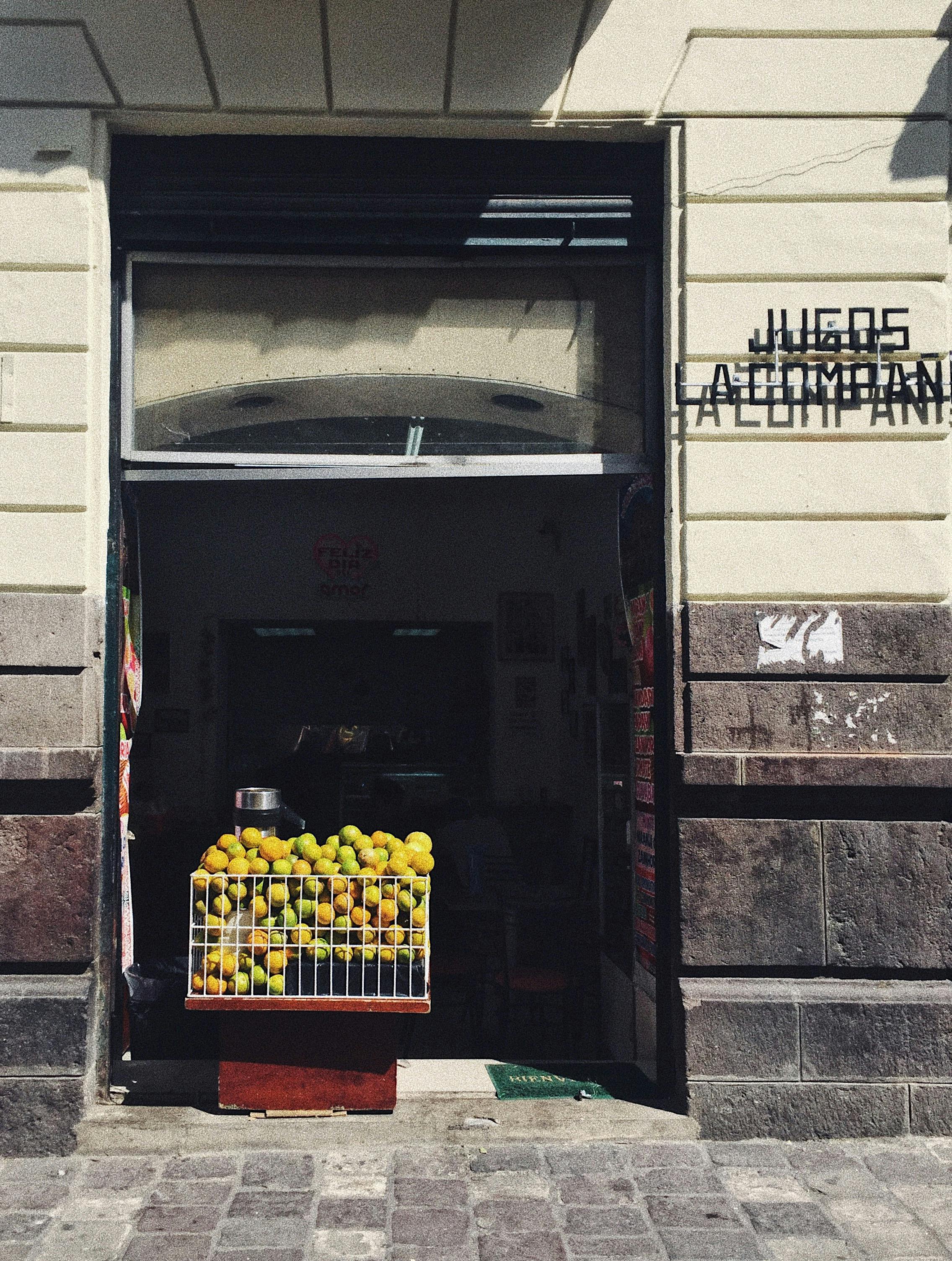 a container with piled green fruit on the doorway of a building