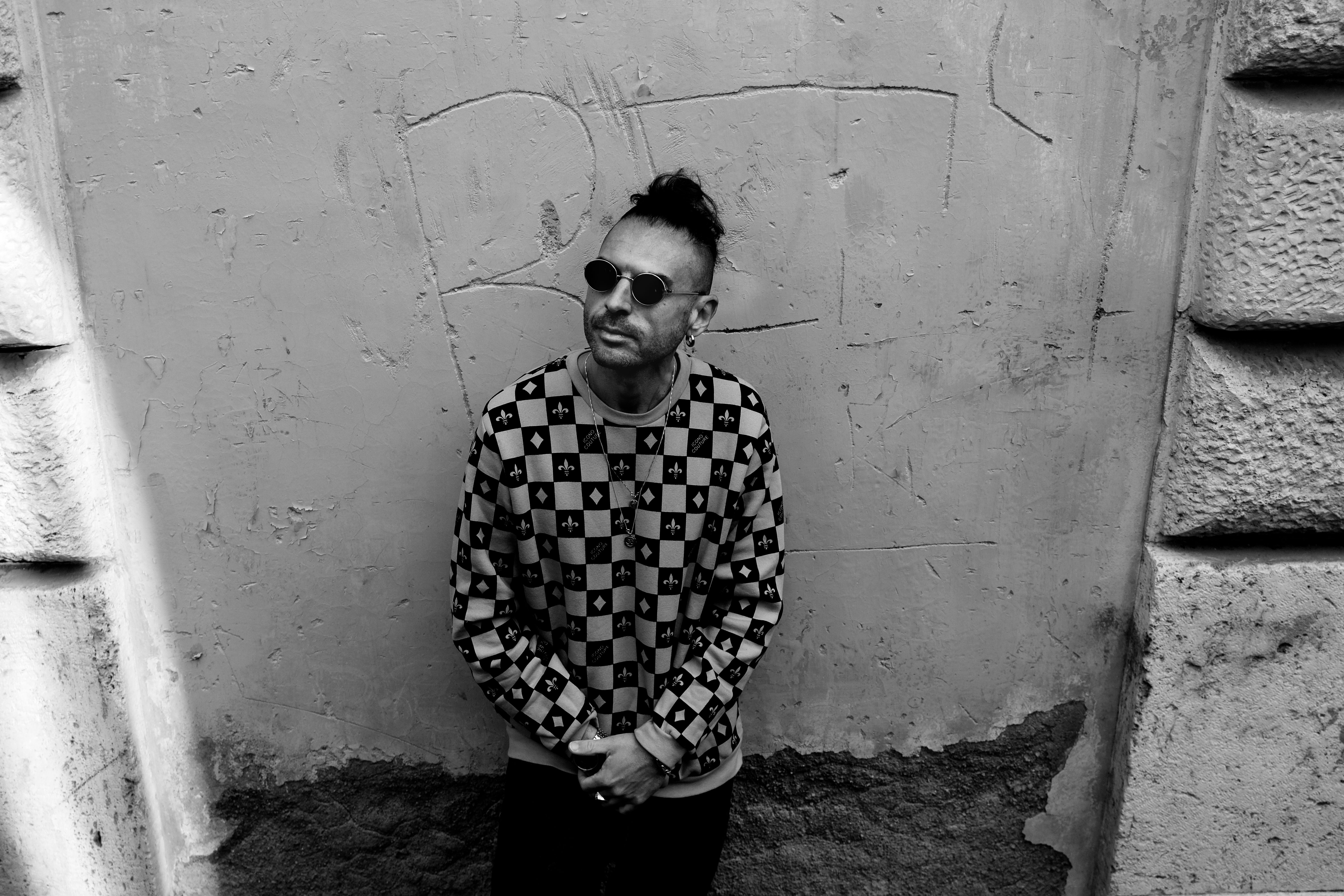 Stylish man in sunglasses stands against textured urban wall.