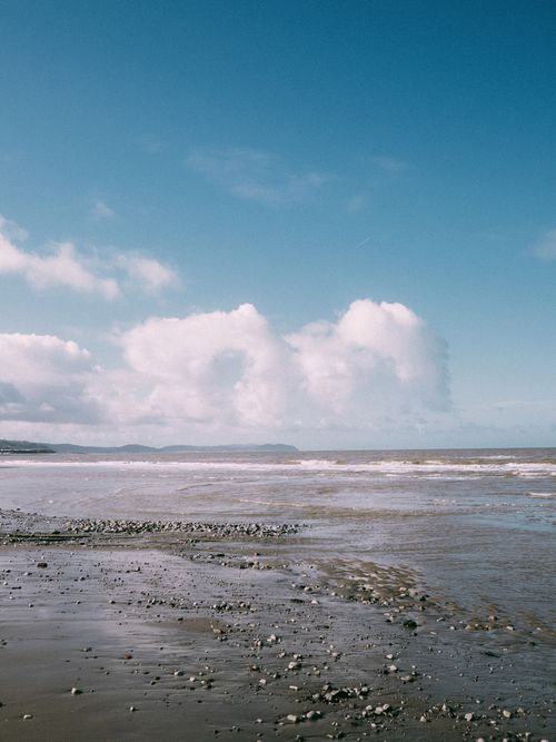 Free Peaceful shoreline with waves and rocks under a bright blue sky, perfect for travel and nature themes. Stock Photo