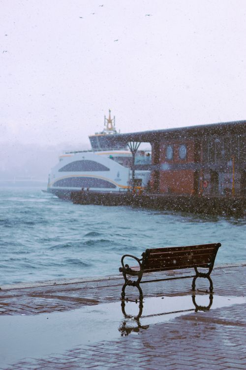 Free A solitary bench facing the water on a snowy day near a docked ferry. Stock Photo