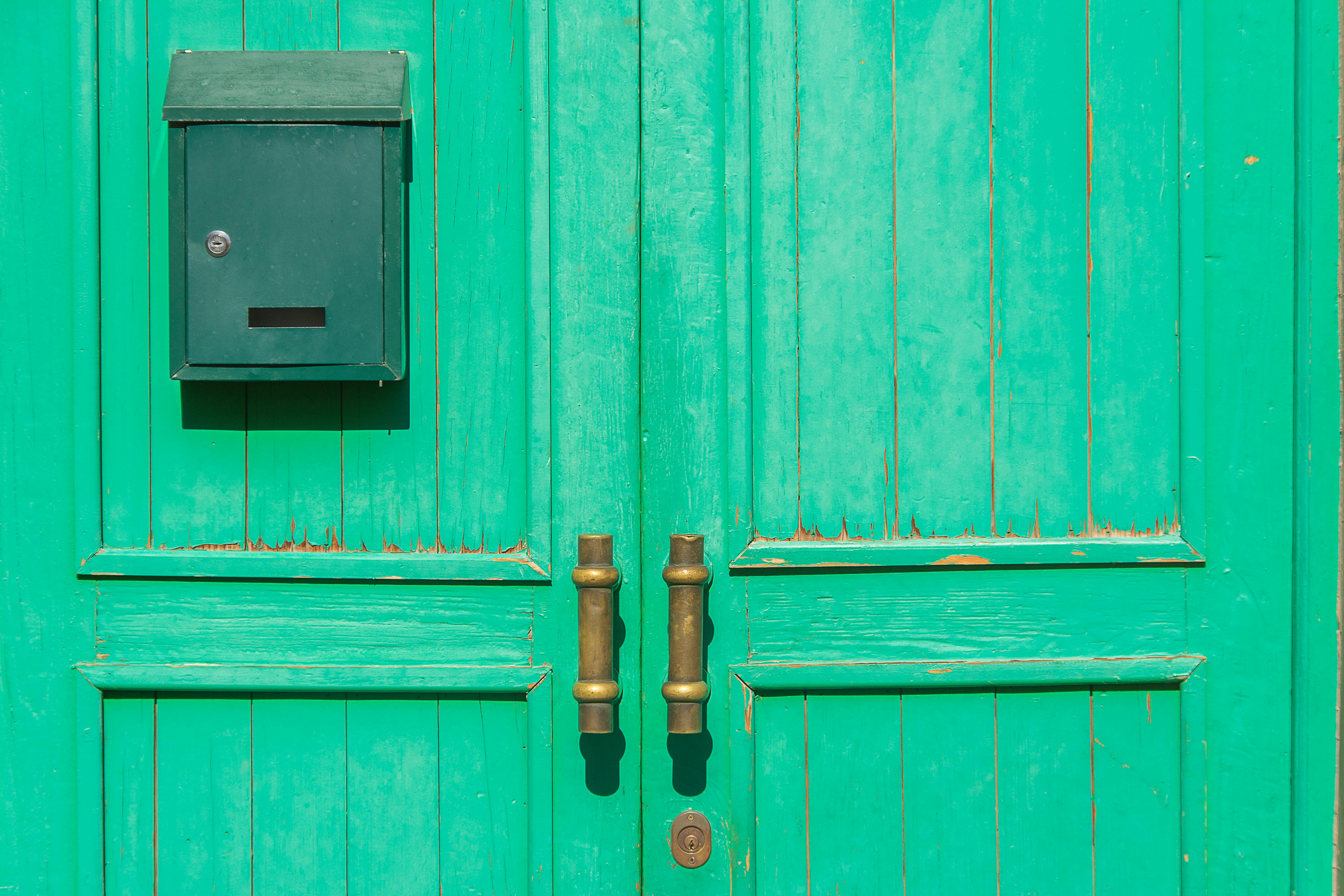 A vibrant green wooden door with brass handles and a matching green mailbox.