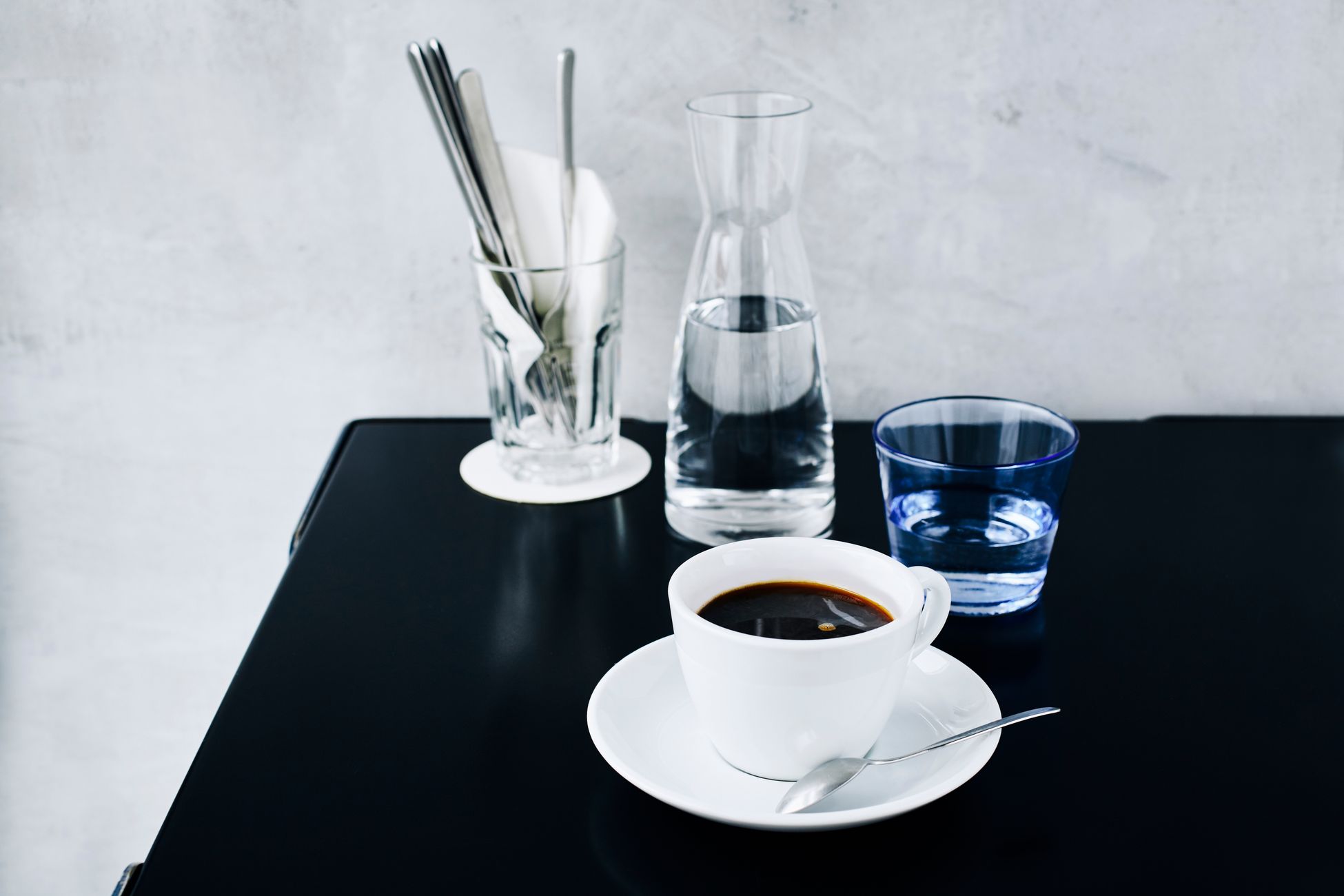 A sleek and minimalist coffee setting with a black coffee, glassware, and utensils.