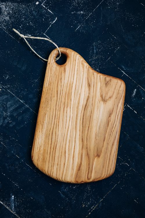 Free Top view of a rustic oak cutting board with string on a textured black background. Stock Photo