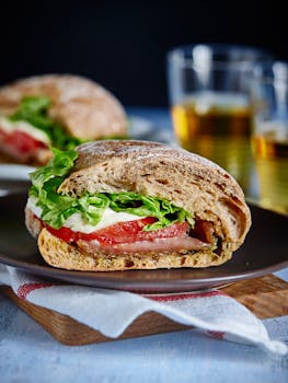 Close-up of a Caprese sandwich featuring fresh tomato, mozzarella, and lettuce on a wooden plate with beer.