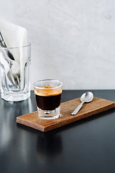 Close-up of an espresso shot served on a wooden board with a spoon.