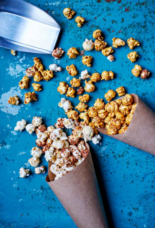 Free Gourmet popcorn scattered from paper cones on a blue surface with a metal scoop. Stock Photo