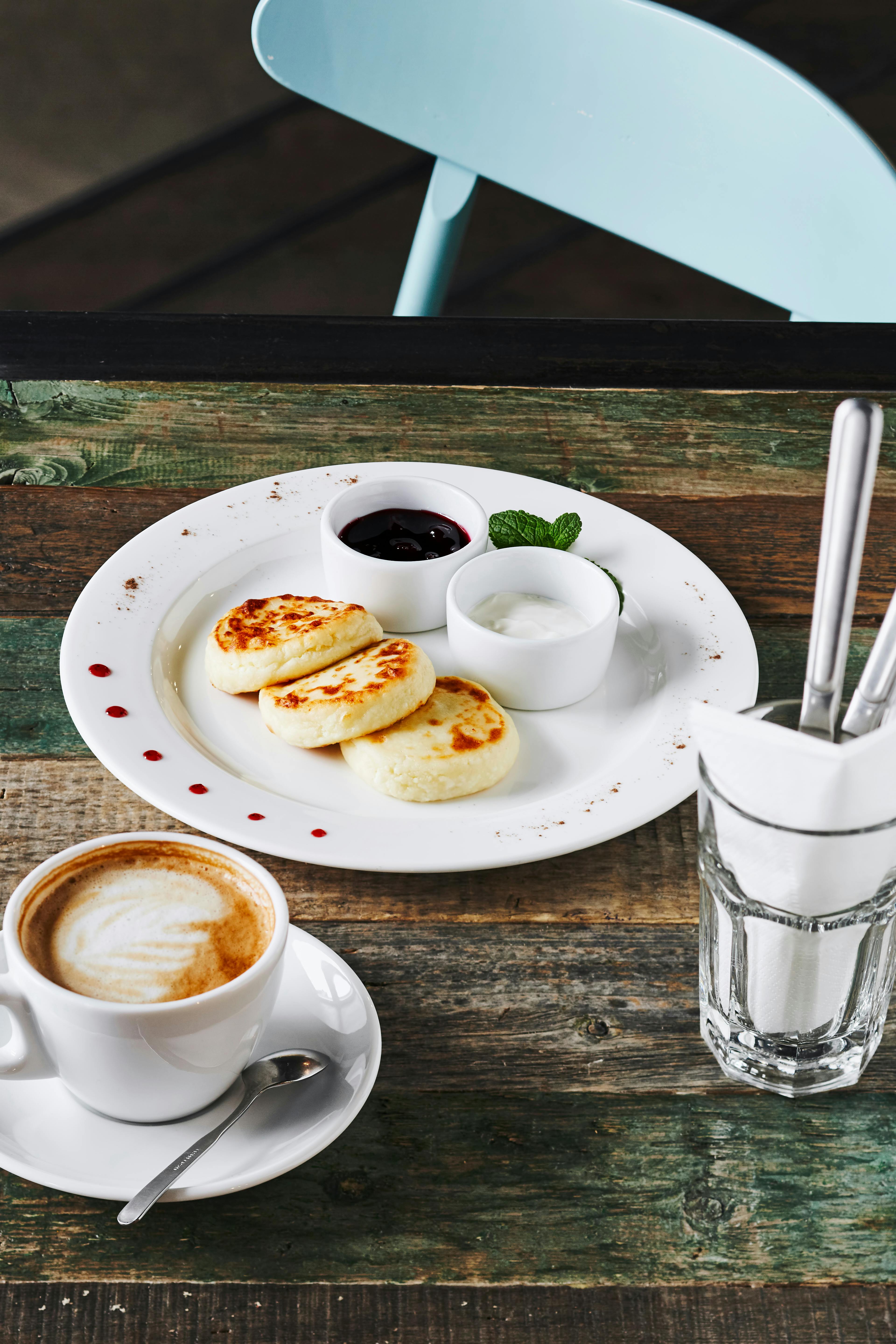 A rustic breakfast setup with cheesecake pancakes, coffee, and cutlery on a wooden table.