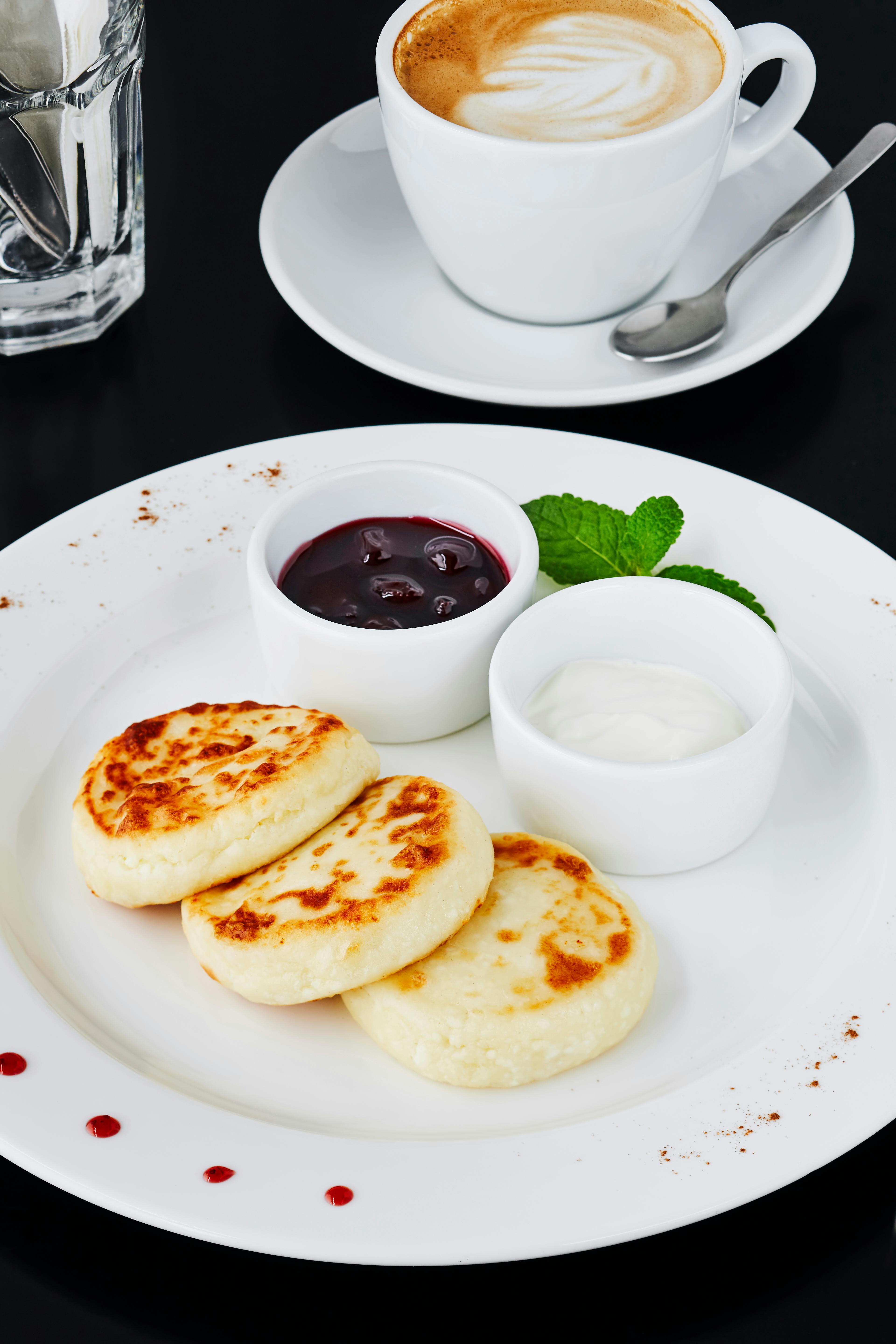 Plate of syrniki with jam, cream, and coffee on a chic café table.