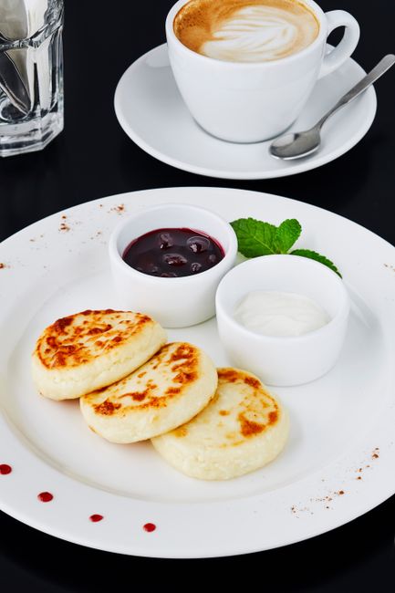 Plate of syrniki with jam, cream, and coffee on a chic café table.