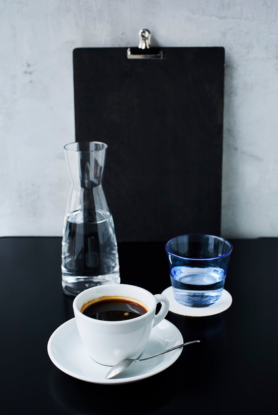 Minimalist coffee setup with a cup, glass, and carafe on a dark table indoors.