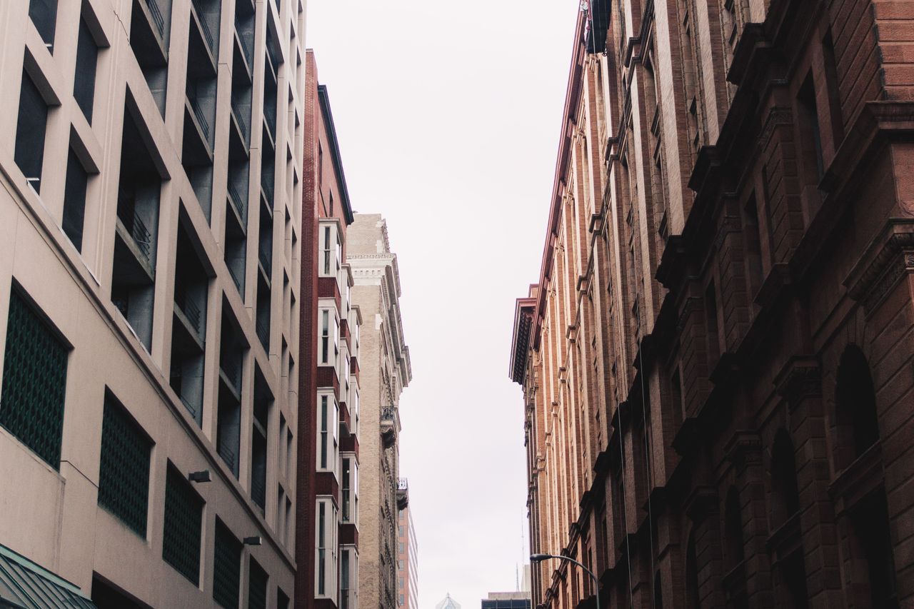 View of tall urban buildings in narrow alleyway with overcast sky.