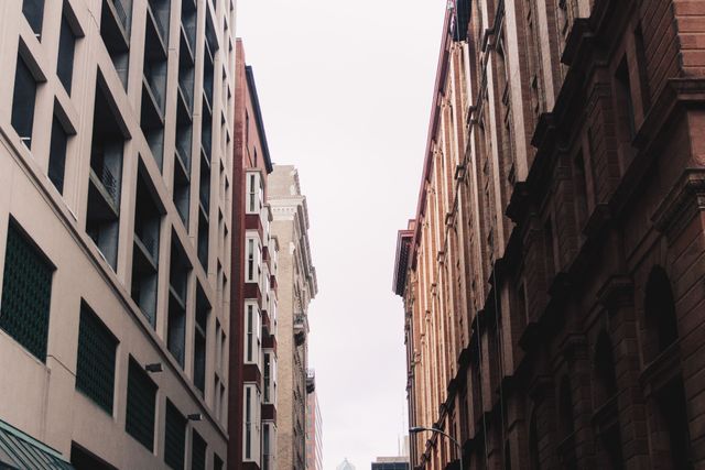 View of tall urban buildings in narrow alleyway with overcast sky.