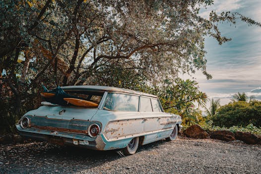 一辆带有冲浪板的经典生锈汽车，停在秋天树木环绕的室外碎石路上