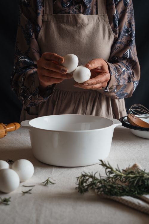 Free Woman cracking eggs into a bowl with herbs on a countertop, preparing for cooking. Stock Photo