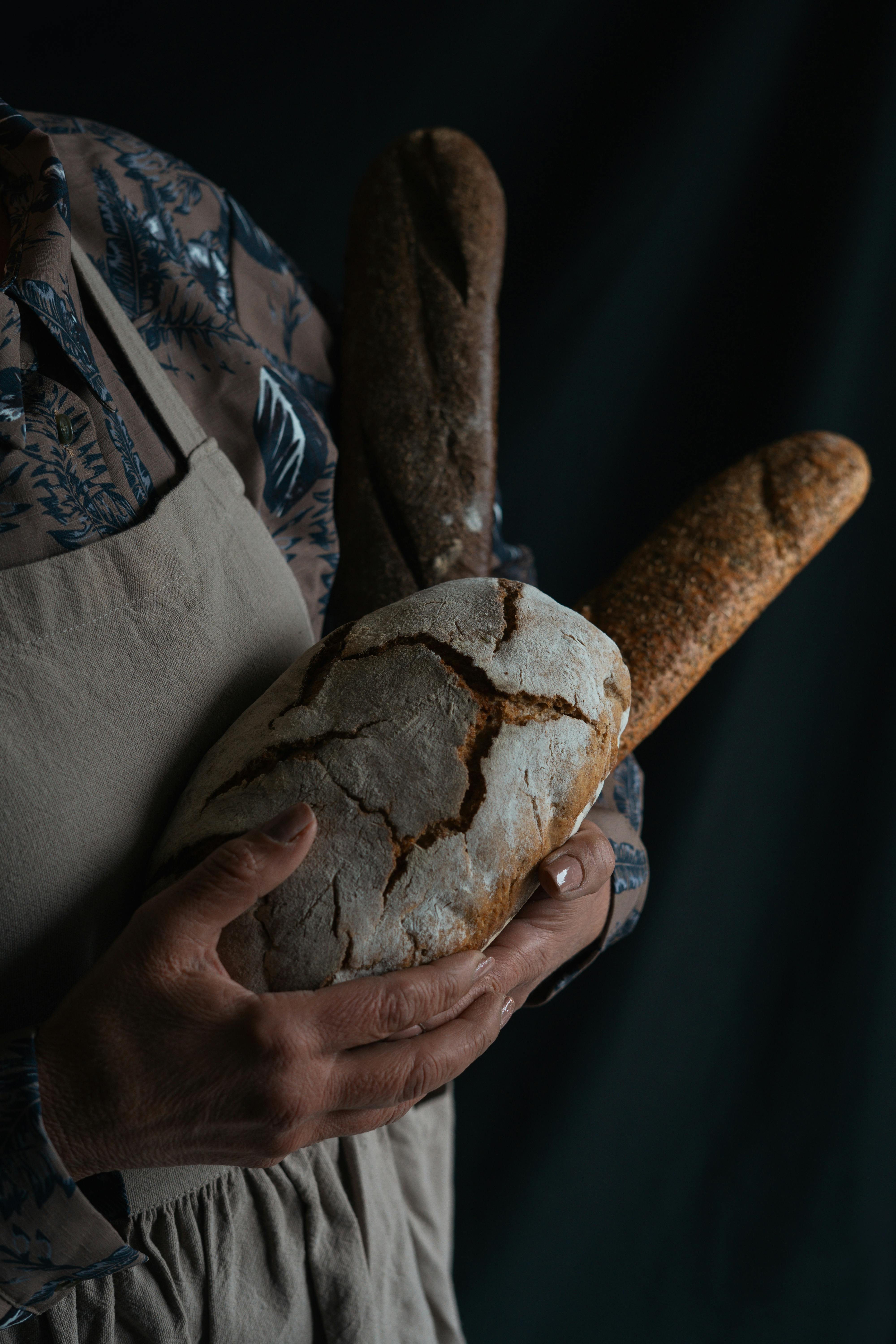 Rustic bread selection held by baker in dim lighting, showcasing artisanal craftsmanship.