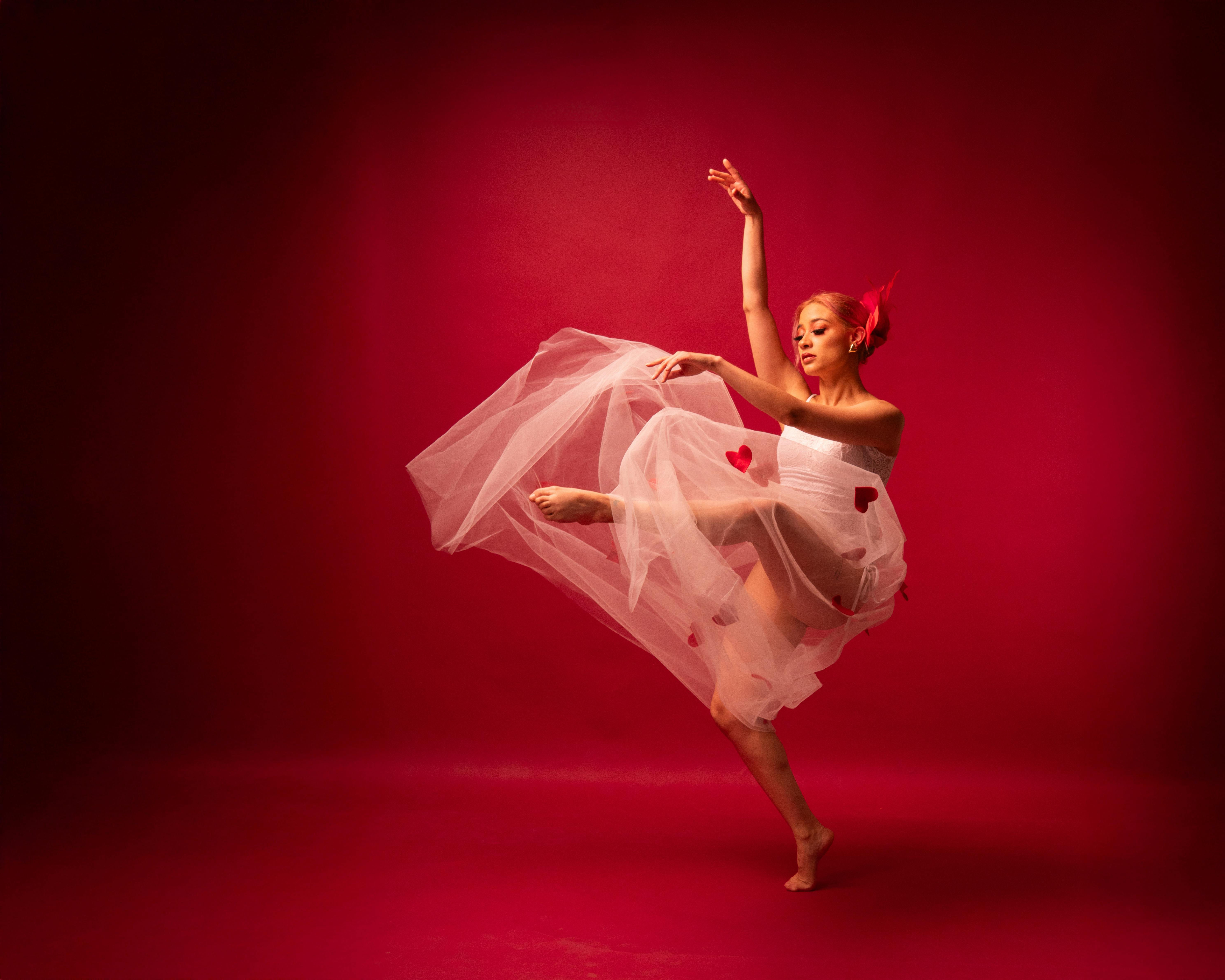 Graceful ballet dancer performing in a white dress with red hearts against a vivid red background.