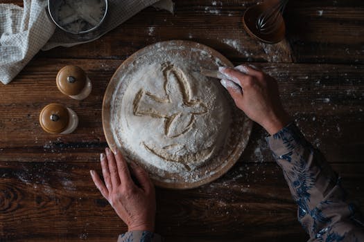 A person carving designs into bread dough on a rustic wood table, highlighting traditional baking.