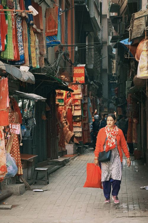 Free A woman strolls along a colorful street market in Nepal, showcasing traditional garments. Stock Photo