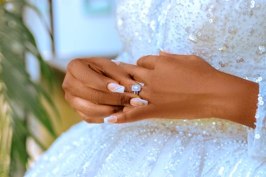 Close-up of a bride's hand showcasing an elegant diamond wedding ring against a beaded white gown.