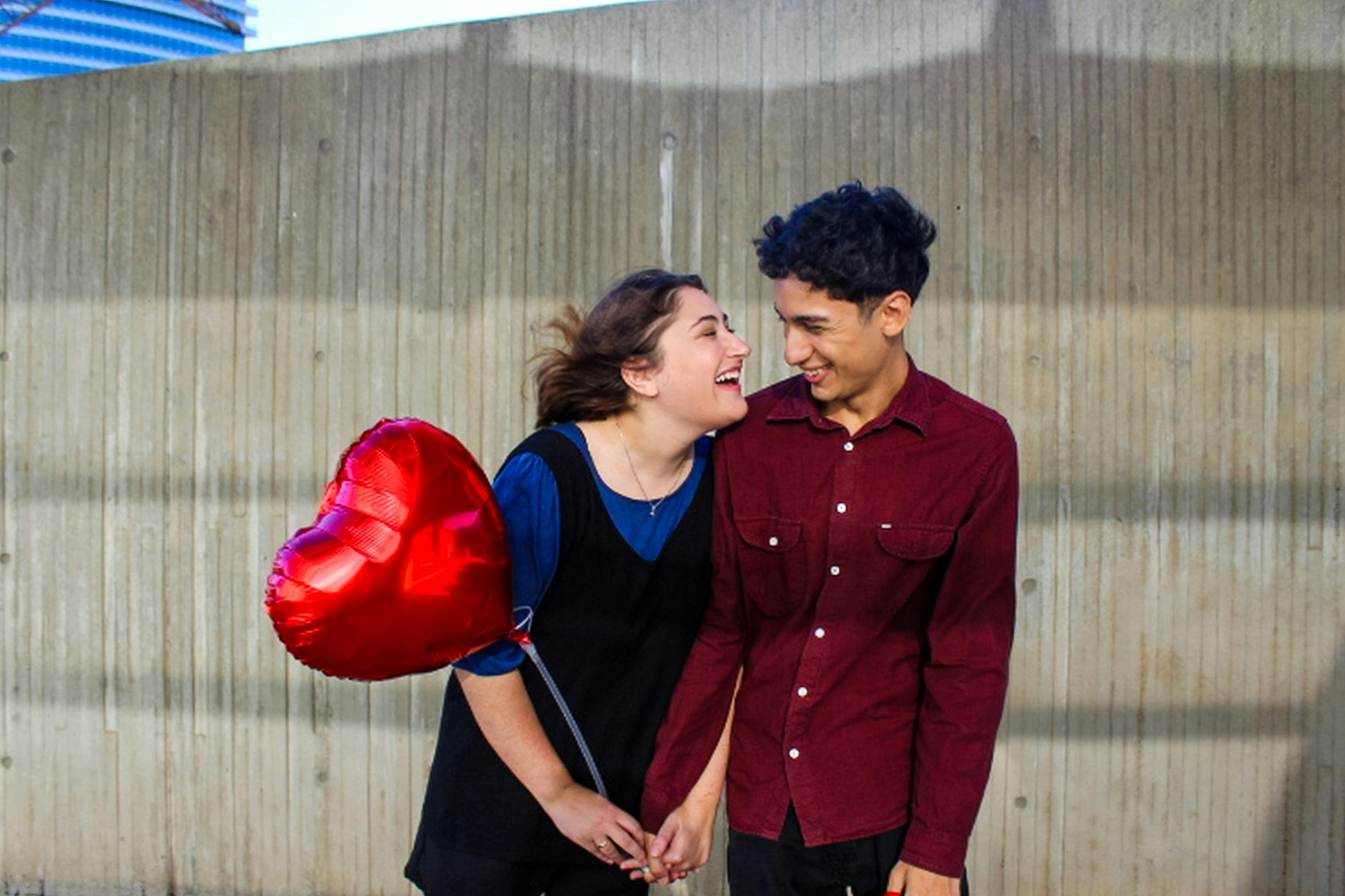 A young couple laughs together holding a heart balloon in Buenos Aires, showing love and happiness.