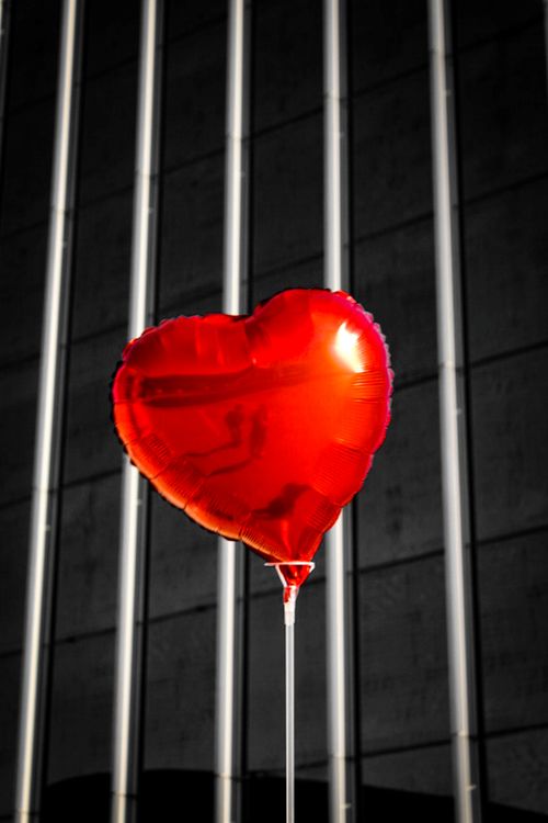 Free A vibrant red heart-shaped balloon floats in front of a modern urban building. Stock Photo