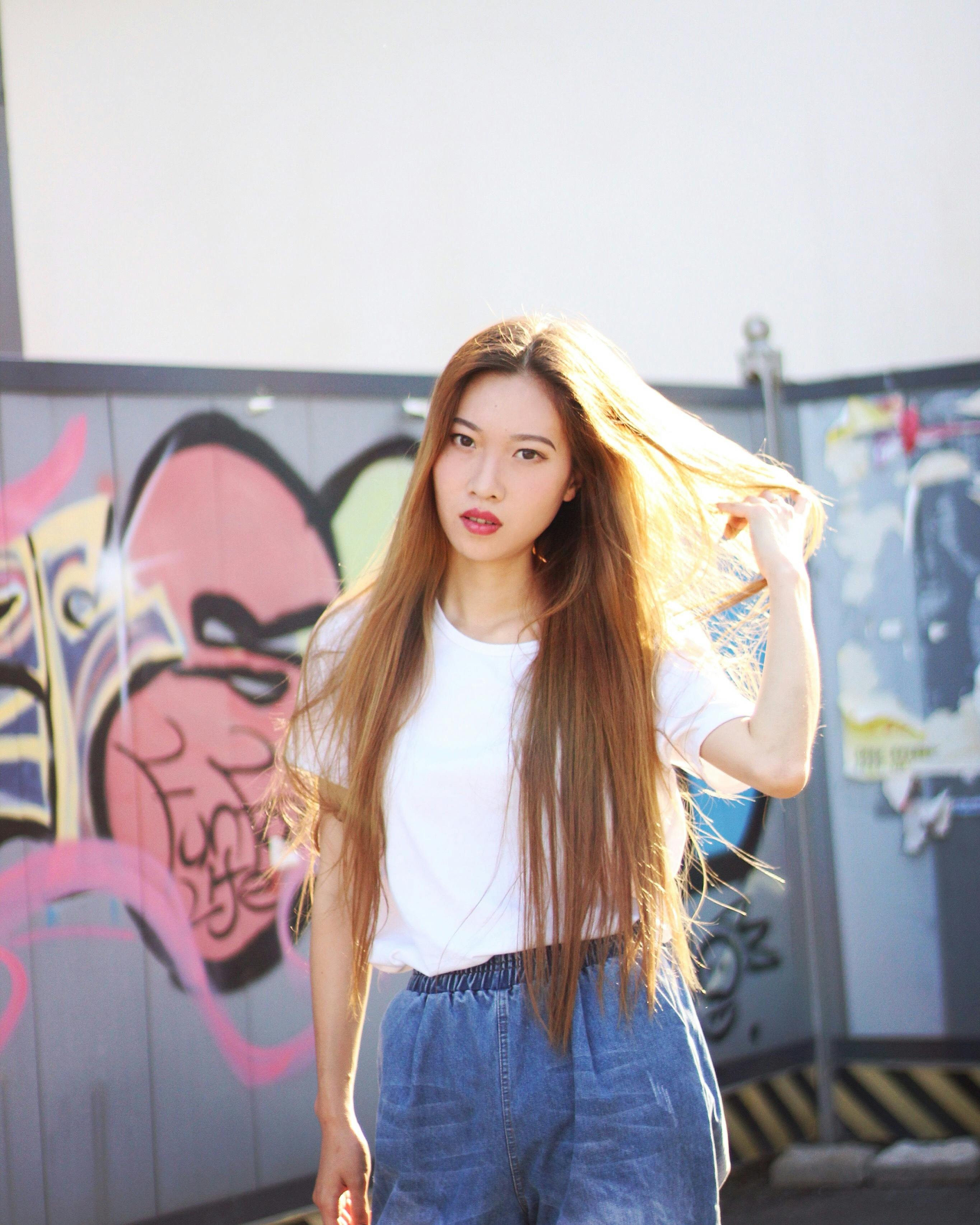 一位时尚女性在五颜六色的涂鸦背景前，自信地摆出休闲装的姿势