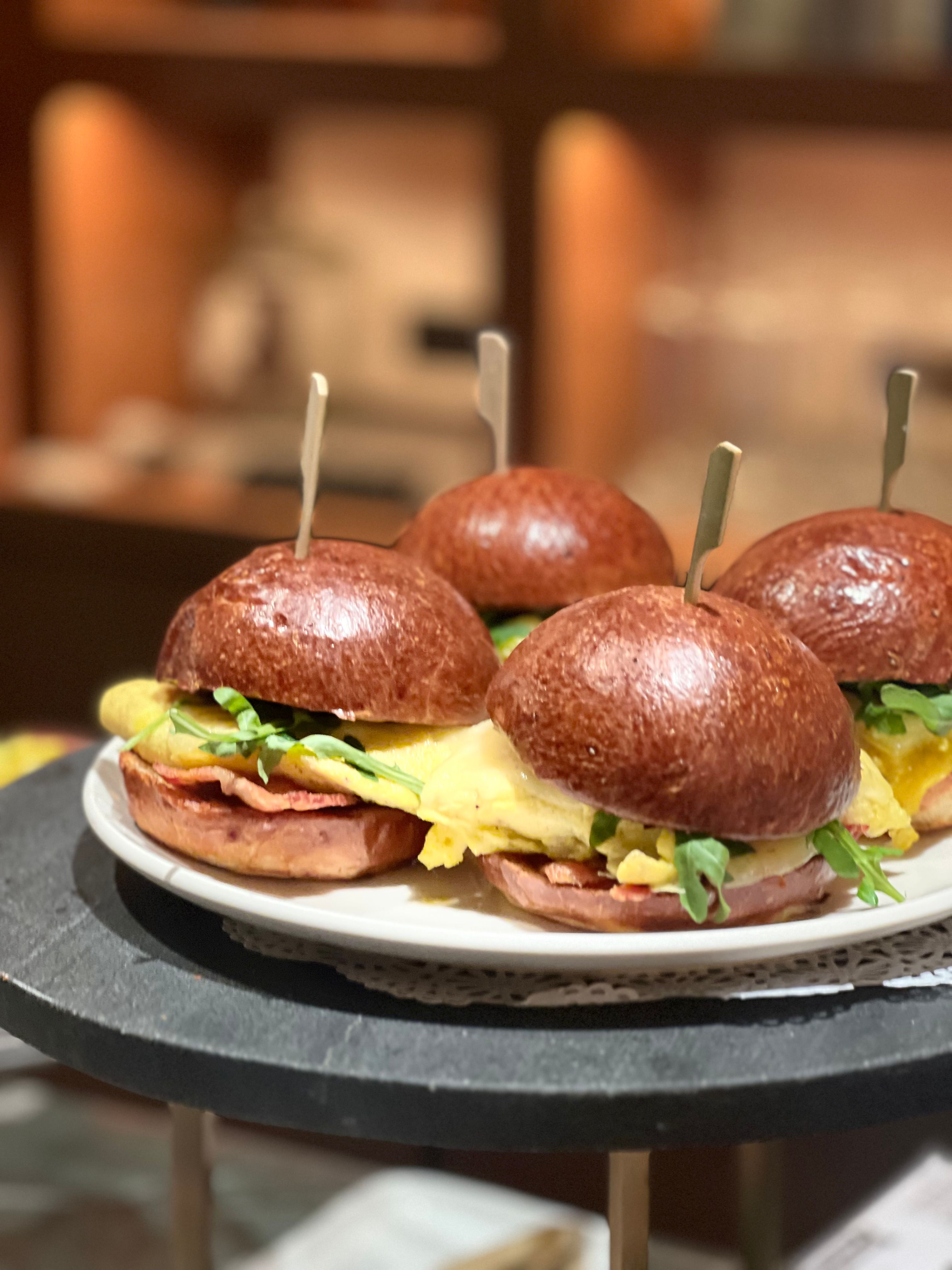 A pan of golden-topped ham and Swiss sliders on soft rolls, one slider lifted out showing melted cheese and thin-sliced black forest ham.