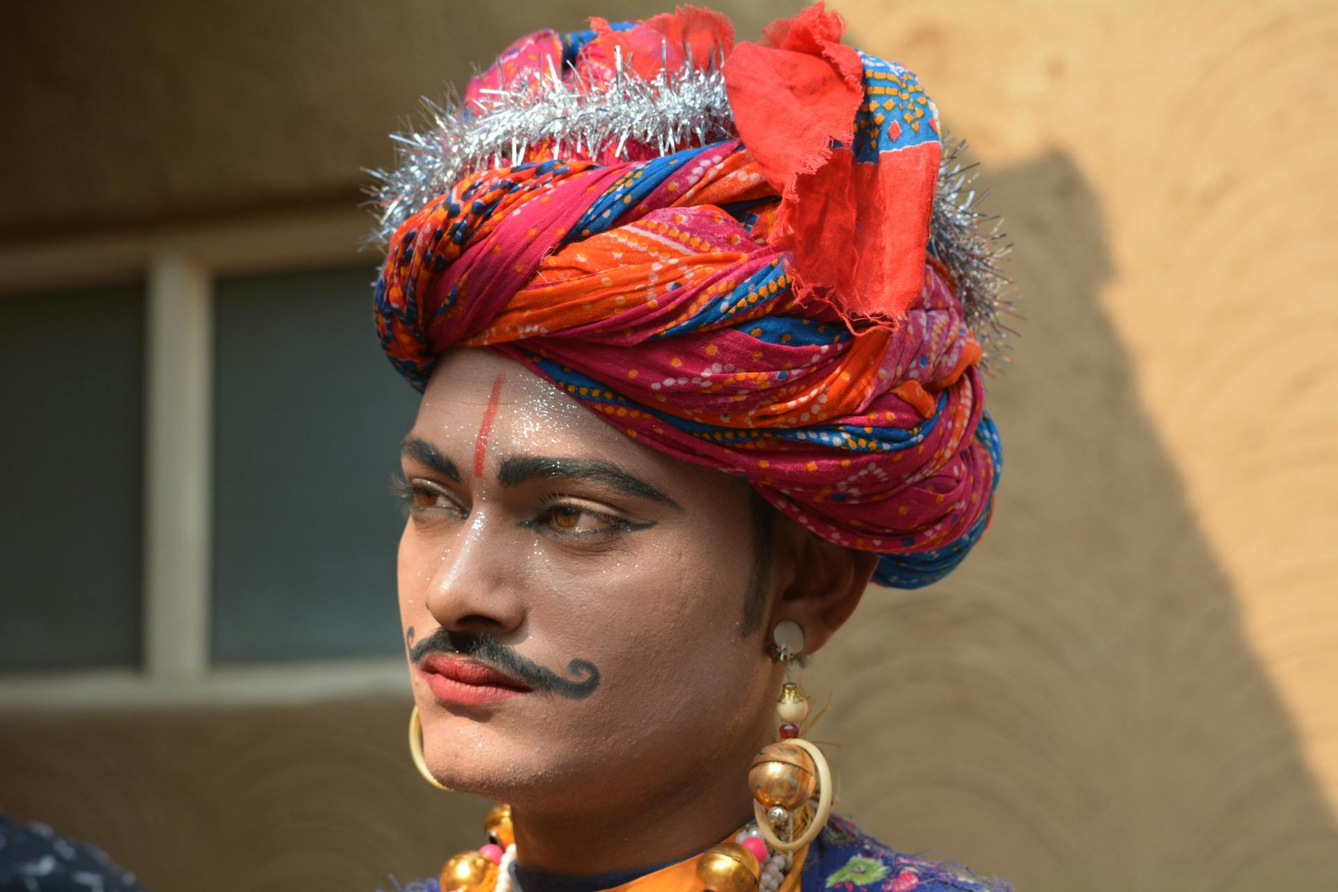 Close-up of a traditional Indian performer with vibrant turban and makeup at cultural fair.