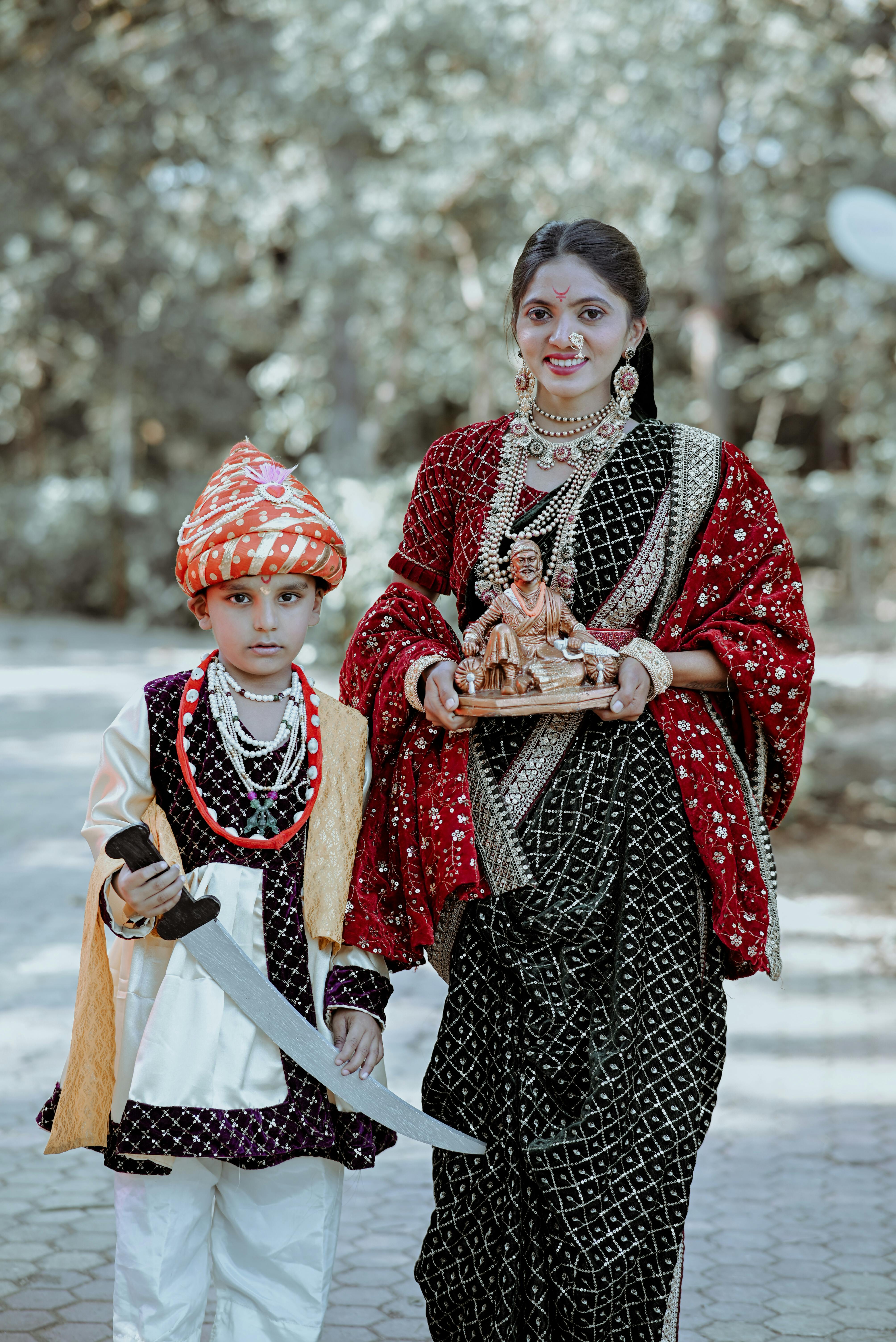 Young boy and woman in traditional Indian attire posing outdoors with cultural artifacts.