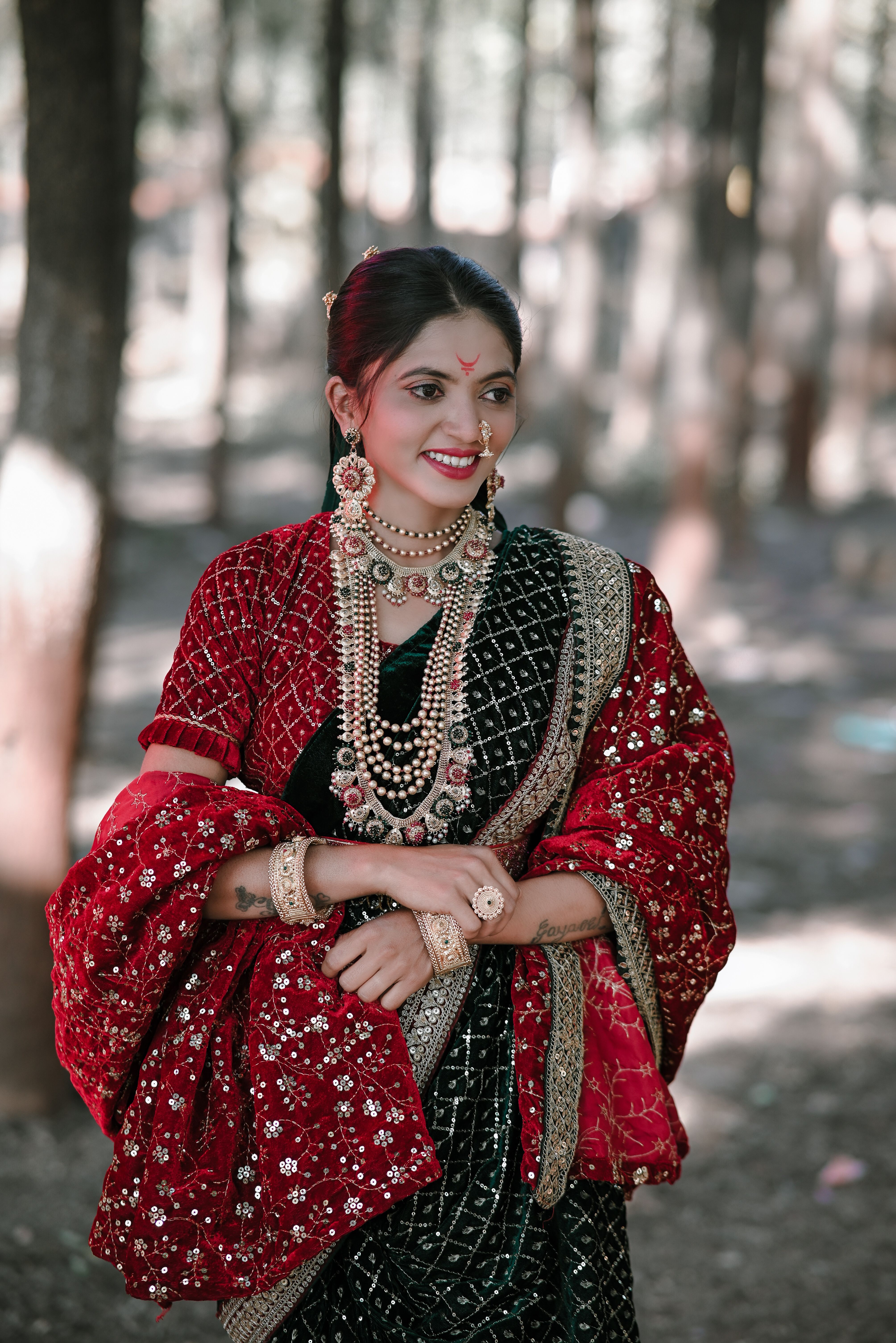 Woman wearing traditional ethnic attire adorned with jewelry in a serene forest setting.