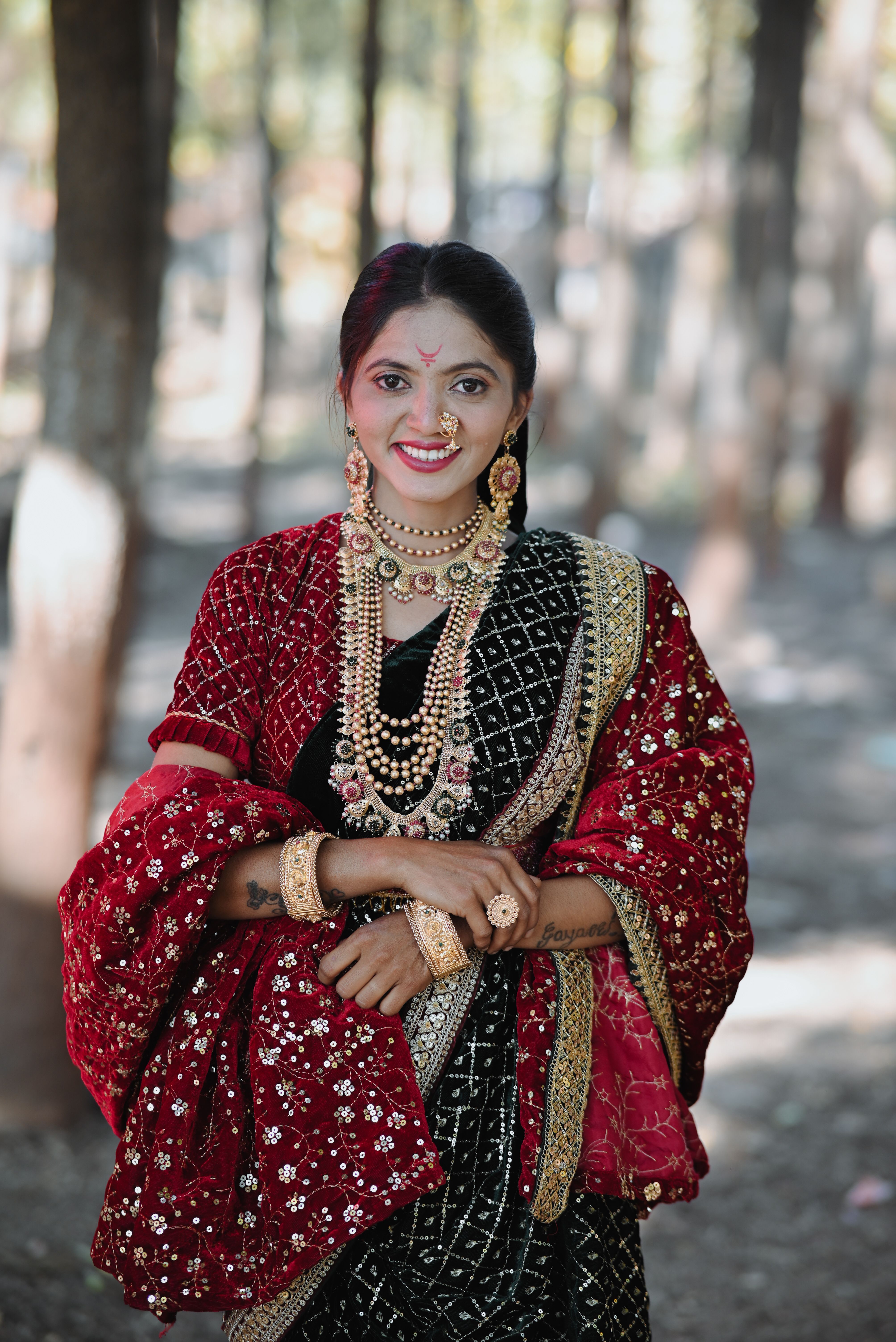 Portrait of a woman in vibrant traditional Indian dress amid forested backdrop, exuding elegance.