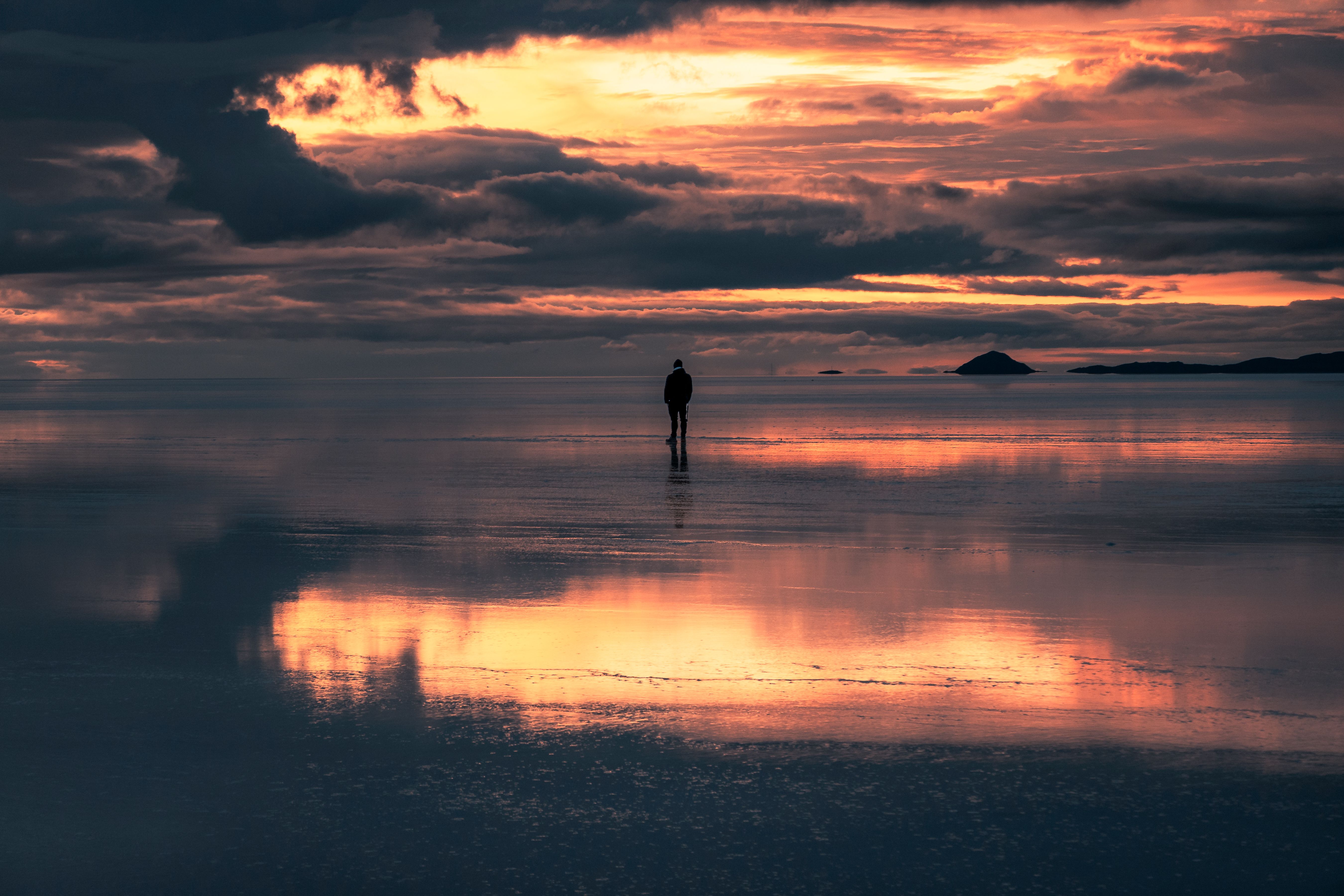 A solitary figure stands at sunset on the reflective surface of Salar de Uyuni, capturing a serene moment.