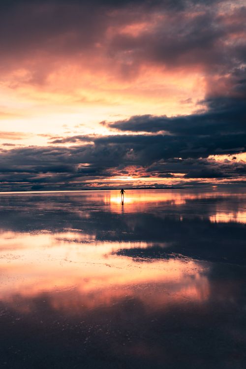 Free A lone figure stands amidst a stunning pink and orange sunset at the Uyuni Salt Flats in Bolivia. Stock Photo