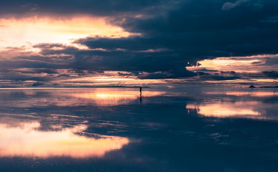 A lone person stands amid the stunning sunset reflection on Uyuni's salt flats in Bolivia.