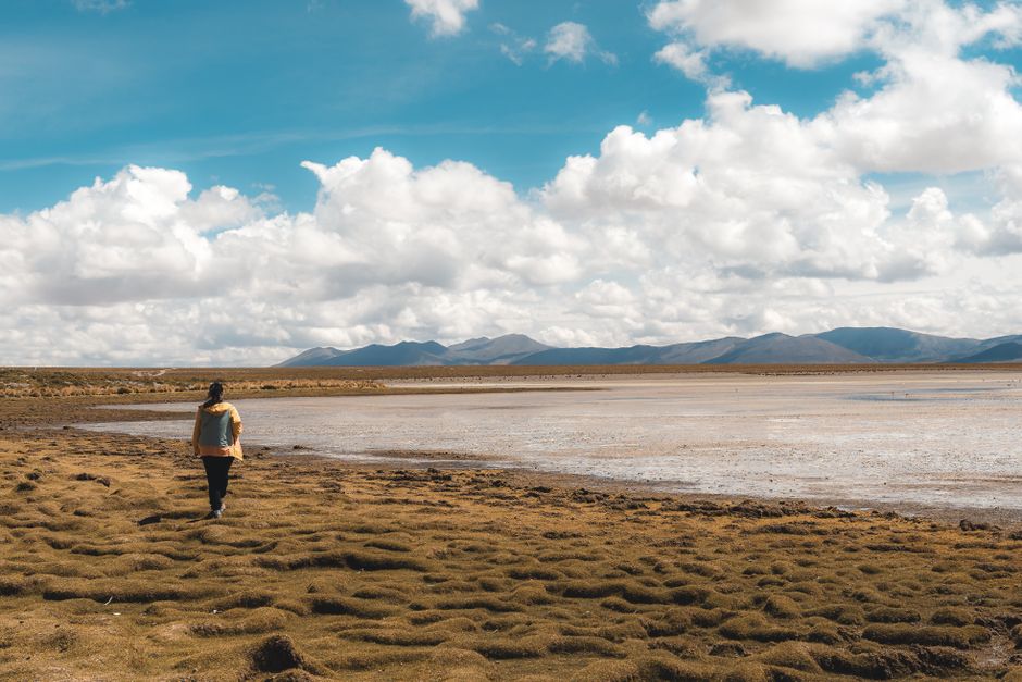A lone traveler walks by the vast salt flats of Uyuni, Bolivia under a bright sky.