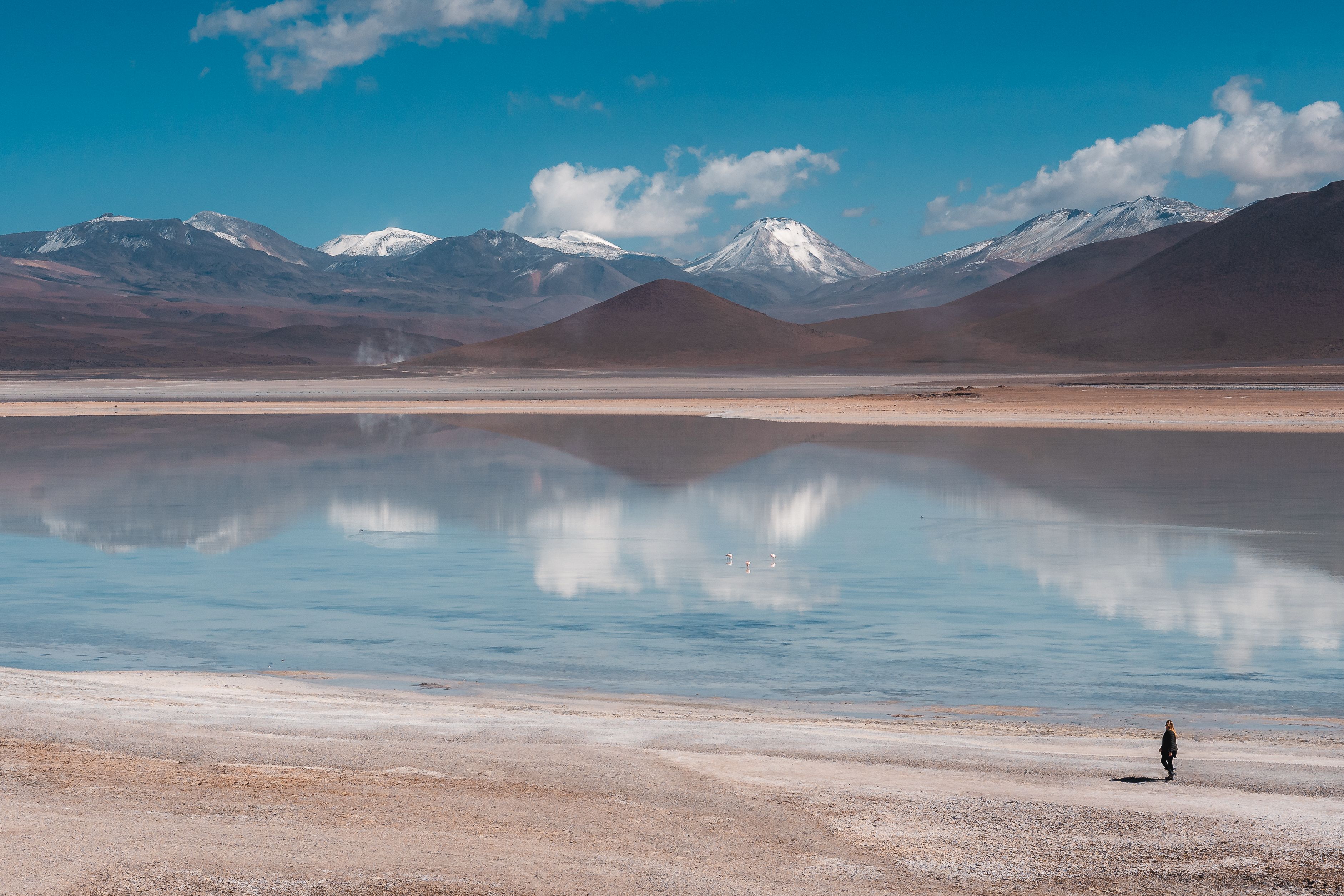 Stunning view of the Uyuni Salt Flats reflecting the Andes Mountains under a bright blue sky.