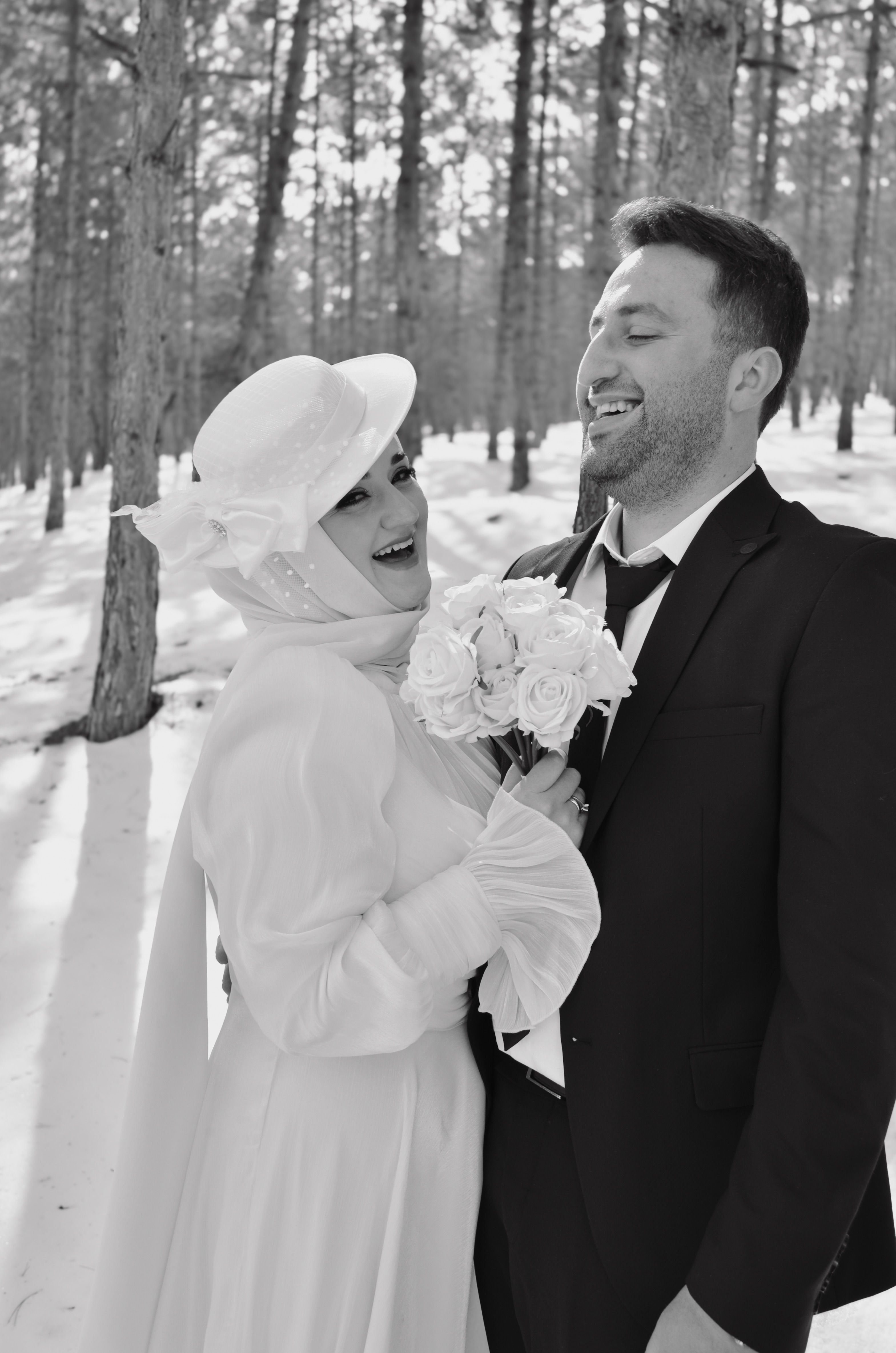 Elegant bride and groom share joyful moments in a snowy forest setting.
