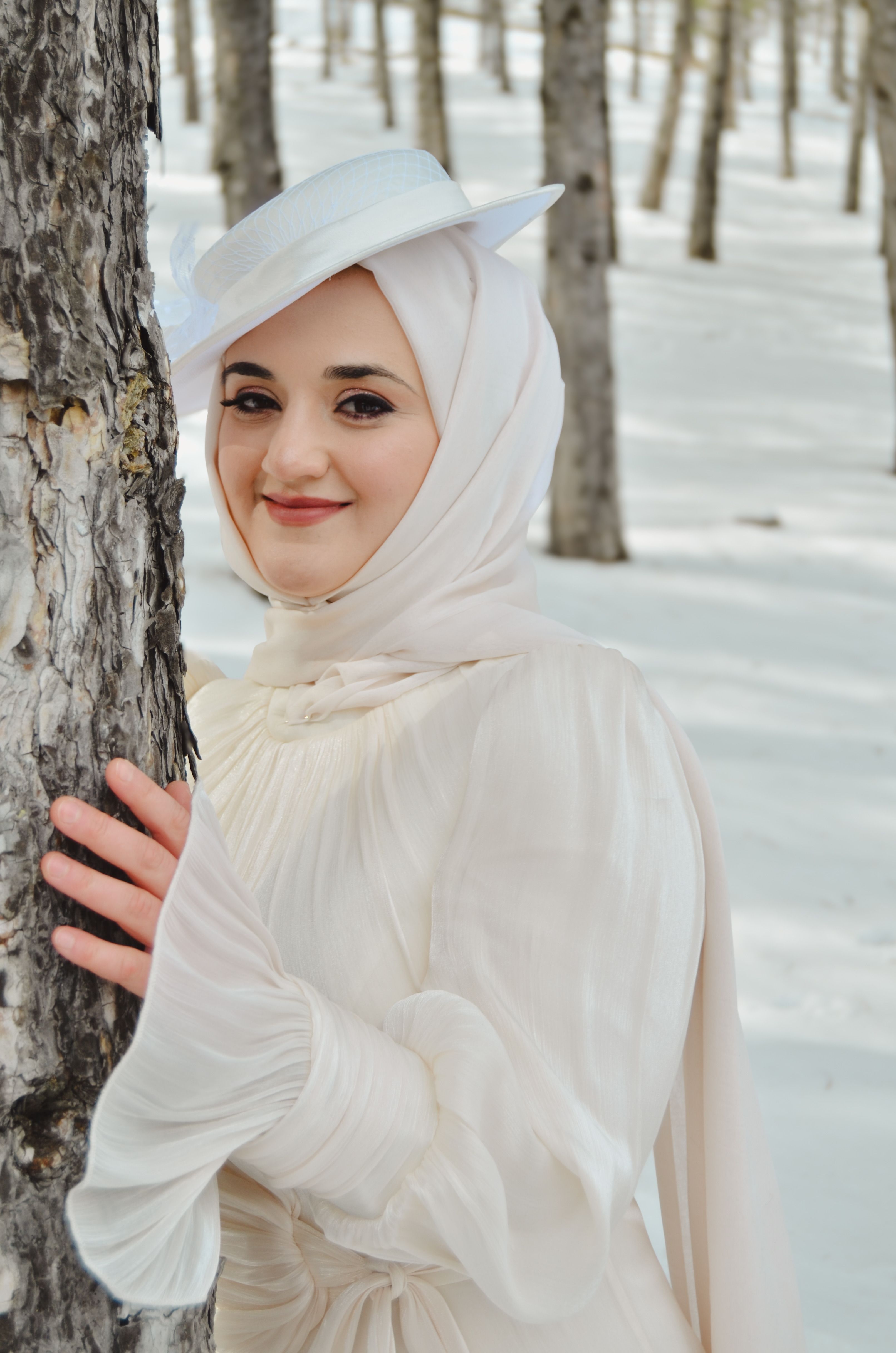 A stunning bride poses amidst a serene, snowy forest in elegant white attire.