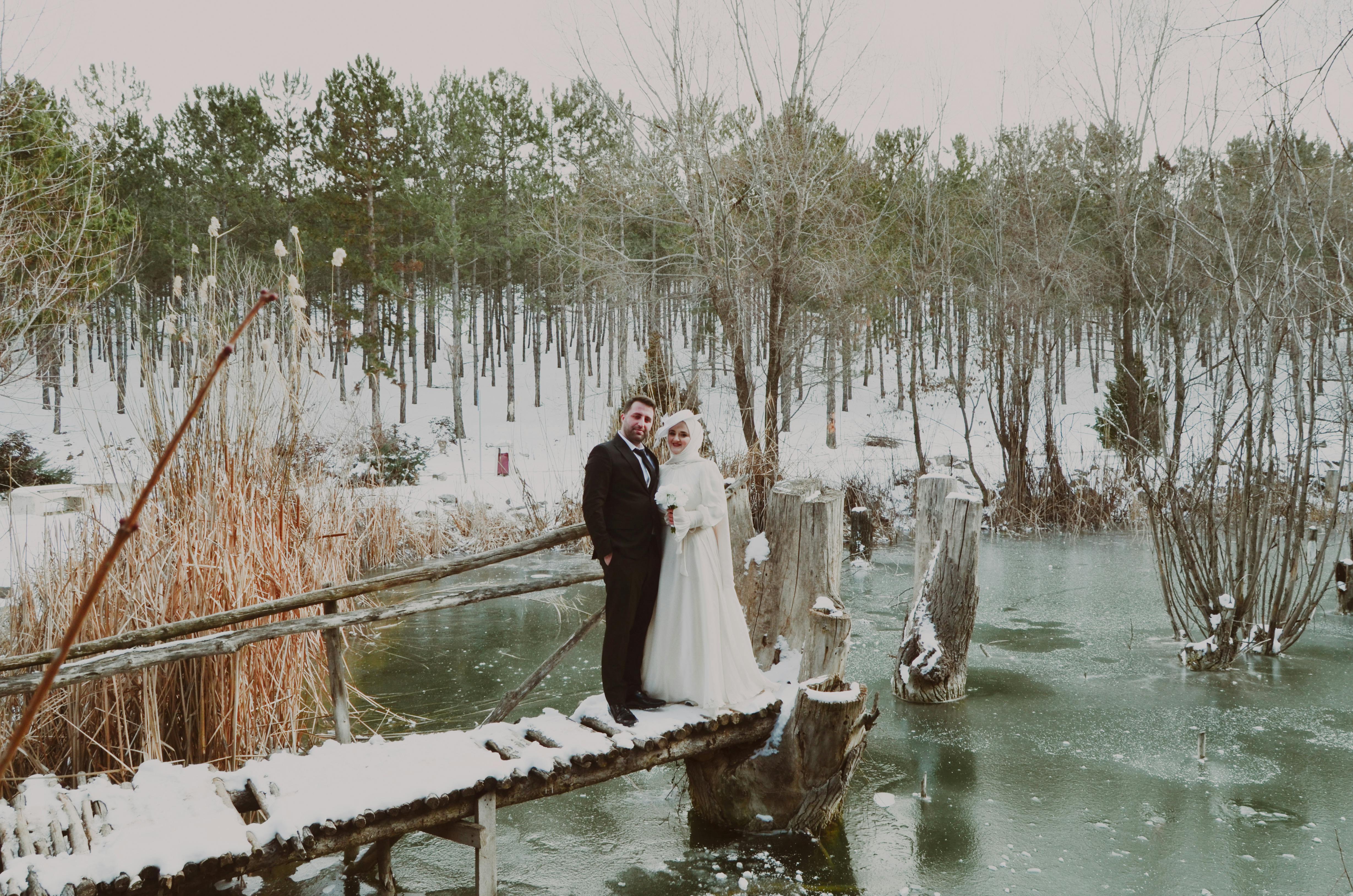 Kar yağışı altında rustik ahşap masa düzenlemesi, altın şamdanlar, bordo güller ve çam kozalakları ile süslenmiş kış düğünü dekorasyonu